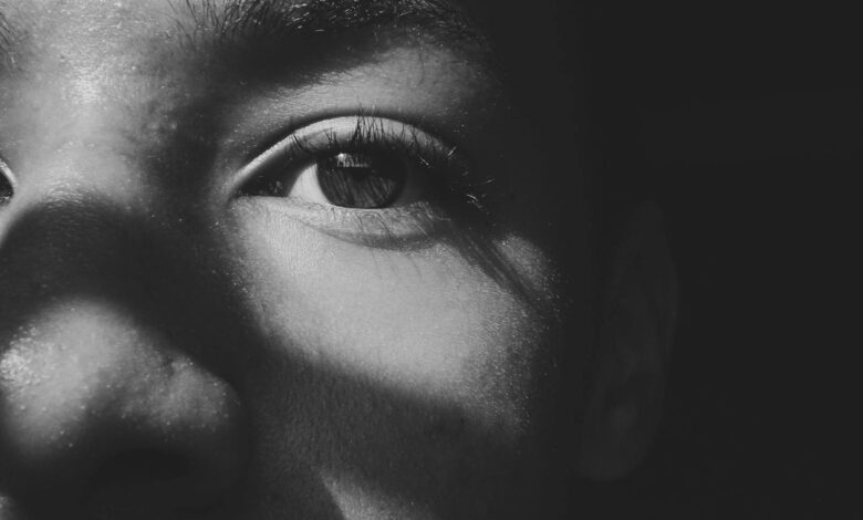 Close-up black and white photo of a person's eye with dramatic shadows casting across the face.